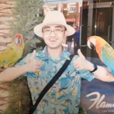 Dr. Dao Yuan Han, Chief Data Officer of Wolfe Services, giving two thumbs up between two macaws